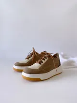 Championes de cuero color visón con cordones marrones, suela blanca y base color caramelo.