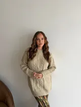Buzo de punto en color beige, con diseño de trenzas verticales en el frente, cuello redondo y mangas largas con puños acanalados.