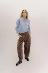 Pantalón de lino y algodón color marrón, de tiro medio o bajo, con pinzas frontales y pretina ancha en la espalda con cambio de color y vivo en contratono. Presenta cortes en la mitad de la pierna trasera, cierre frontal con cremallera y botón, y bolsillos delanteros.