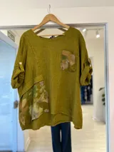 Blusa verde pistacho de lino, con cuello redondo, mangas tres cuartos con presilla y botón, y detalles estampados florales en el bolsillo pectoral y en la parte inferior.