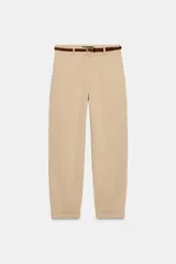 Pantalón chino beige de tiro bajo, con pernera recta y bajo con vuelta. Incluye bolsillos delanteros, falsos bolsillos traseros con solapa y cierre frontal con cremallera y botón. Viene acompañado de un cinturón trenzado marrón.