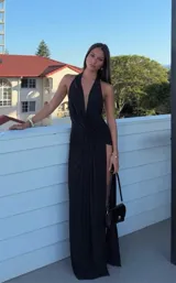 Vestido largo negro de fiesta con escote profundo tipo halter, diseño drapeado en la cintura y tajo lateral profundo en la falda.