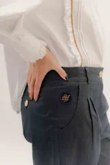 Pantalón sastrero de tiro medio, color gris oscuro con rayas verticales finas. Presenta pinzas delanteras, bolsillos delanteros con pin bordado y bolsillos traseros tipo vivo.