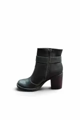 Bota corta de cuero color negro, con taco cuadrado y puntera redondeada. Cuenta con una tira con hebilla metálica plateada alrededor del tobillo y costuras visibles a contratono.