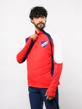 Buzo de entrenamiento Umbro del Club Nacional de Football, con cierre frontal parcial y cuello alto. Presenta un diseño con bloques de color azul, blanco y rojo, con panel frontal acolchado y mangas largas con aberturas para pulgares.