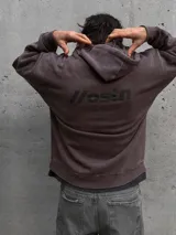 Hoodie de color marrón con efecto acid wash, capucha con cordones ajustables, bolsillo canguro frontal y pequeño estampado con texto en el pecho. Cuenta con una etiqueta decorativa en el borde inferior.