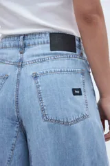 Jean de mezclilla celeste claro, tiro medio, con corte extremadamente ancho y acampanado desde la cadera hasta el bajo, con costuras verticales que acentúan la amplitud de la pierna.