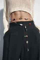 Pantalón de lino negro de tiro medio, con pernera recta, pinzas delanteras y detalle de puntilla en la cintura. Cuenta con bolsillos frontales y cierre con cremallera y botón.