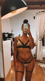 Conjunto de lencería de cuatro piezas compuesto por bralette, tanga, portaligas y ligas. Confeccionado en lycra beige con detalles de encaje negro en los bordes y tiras elásticas decorativas.