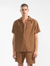 Bermuda de hombre color azul petróleo, confeccionada en mezcla de lino y algodón. Presenta cintura elástica con cordón, bolsillos laterales y trasero tipo parche. Incluye bordado floral en la pierna izquierda y etiqueta con logo en el bolsillo trasero.