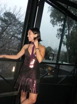 Vestido corto de tela metalizada en tono fucsia con reflejos dorados, con escote en V, diseño de top con triángulos, aberturas laterales en la cintura y doble volado irregular en el ruedo.
