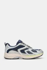 Zapatilla deportiva estilo running con combinación de materiales y colores. Presenta paneles en azul marino, plateado y detalles en amarillo neón, con suela de plataforma en tono beige y tirador en el talón.
