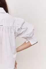 Camisa azul marino de cuello clásico, mangas abullonadas a tres cuartos y detalle fruncido en el frente. Presenta una silueta amplia y diseño corto con vuelo en el ruedo.
