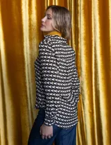 Camisa negra de gasa con estampado de caballos blancos y marrones. Tiene cuello con solapa y abertura central con botones.