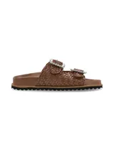 Sandalias planas marrones de cuero entrelazado, con dos tiras ajustables con hebillas grandes decoradas con pedrería brillante y suela de EVA con base dentada negra.