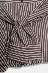 Bermuda de tiro medio con estampado de rayas verticales en tonos marrones y celestes. Presenta un diseño único con lazada frontal que simula mangas anudadas, elástico en la parte posterior de la cintura, cierre frontal con cremallera y botones, y bajo con vuelo.
