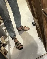 Sandalia de cuero marrón con tiras finas y detalles de tachas doradas. Tiene un pequeño taco cuadrado y cierre con hebilla dorada en el tobillo.