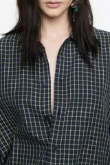 Camisa larga de corte recto, confeccionada en algodón, con patrón de cuadros pequeños en tonos azul marino y amarillo claro. Presenta cuello camisero, cierre frontal con botones y mangas largas con puño y botonadura.