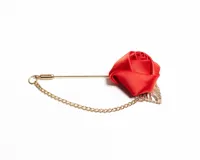 Pin para el ojal con diseño de flor de tela satinada roja y hoja metálica dorada, unido por una cadena fina de metal dorado.