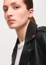 Chaqueta biker de piel de ovino color negro, con diseño recto, solapas con muesca, bolsillos laterales y frontal con cremallera, y forro interior de poliéster.