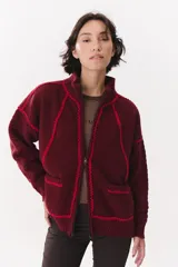 Campera de tejido de punto color marrón con destellos de lurex, corte oversize y cierre frontal. Presenta detalles de costuras y terminaciones en color crema, cuello alto y bolsillos frontales.