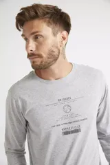 Remera de manga larga color gris melange, con cuello redondo y estampa frontal con diseño gráfico y texto.