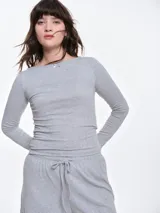 Remera de manga larga entallada en tejido pointelle, con escote bote y detalle de pequeño lazo central. Presenta un acabado con borde picot en el escote.