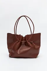 Bolso tipo tote bag color marrón, con frunce superior ajustable mediante cordón. Tiene doble asa corta de mano.