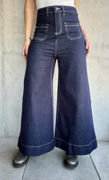 Pantalón de jean azul oscuro, de corte ancho, con bolsillos delanteros cuadrados y costuras blancas contrastantes.