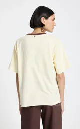 Remera de algodón color beige con cuello redondo en contraste marrón. Presenta mangas cortas y un estampado frontal con temática western que incluye letras y una ilustración central.