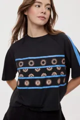 Remera blanca de manga corta, con cuello redondo, calce relajado y estampado frontal con motivos gráficos de soles y símbolos marinos en tonos rosados y bordo, además de líneas horizontales.