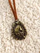 Collar con dije de escudo patrio en tono bronce envejecido, sujeto por un cordón de cuero marrón.