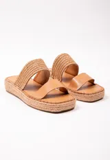 Sandalia con doble tira en el empeine, una de cuero color tostado y otra tejida en rafia. Plataforma de yute de 3.5 cm de alto.