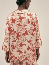 Camisa de manga 3/4 confeccionada en seda viscosa con estampado floral en tonos naranja, rosado y marrón sobre fondo azul marino. Presenta un diseño de corte holgado, cuello camisero y cierre frontal con botones.