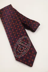 Corbata de poliéster color borgoña con estampado geométrico y logo de la marca serigrafiado en blanco.