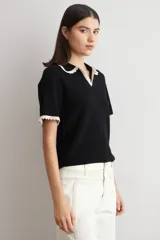 Sweater de punto negro de manga corta con cuello polo y ribetes contrastantes en color beige con detalles de encaje en el cuello y los puños.