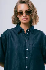 Vestido corto de denim azul oscuro, con cuello camisero, mangas cortas, cierre frontal con botones, bolsillo aplicado en el pecho y calce holgado.