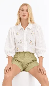 Camisa blanca de lino natural con bordados artesanales de flores en el frente y mangas abullonadas de largo tres cuartos.