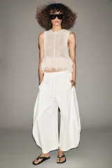 Chaleco de punto calado color crudo, de cuello redondo y sin mangas. El bajo está terminado con flecos.