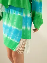 Minifalda de tejido de red teñida con técnica batik en tonos verde y celeste, con flecos y canutillos en un lateral.