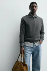 Polo de manga larga color gris oscuro, con diseño de textura estructurada, cuello solapa y cierre frontal de cremallera corta. Cuenta con puños y cintura de rib elástico.