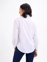 Camisa blanca de manga larga con cuello camisero, cierre frontal con botones y detalles de tablas verticales en el frente.
