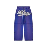 Pantalón baggy color azul con efecto lavado, presenta un aplique bordado con la palabra 'Valley' decorado con cristales de colores. Incluye detalles de tachas multicolores a lo largo de las costuras laterales y en el ruedo, cintura elástica con cordón de ajuste y costuras horizontales a la altura de las rodillas.