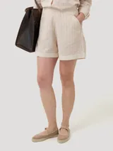 Short de tiro alto color beige con rayas verticales blancas, confeccionado en mezcla de lino y algodón orgánico. Cuenta con bolsillos laterales, botamangas con vuelta y cierre invisible.
