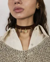 Gargantilla tipo choker de gamuza con dijes colgantes artesanales de metal y perlas naturales. Cuenta con tiras largas para atar y ajustar en la parte posterior.