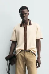 Camisa de punto de algodón con corte relajado, cuello solapa y manga corta. Presenta un diseño bicolor en tonos beige y marrón, con cierre frontal de botones.