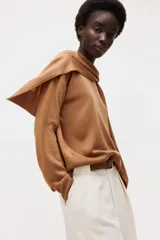 Sweater de punto fino color marrón, de cuello redondo con ribetes en canalé. Presenta un diseño que incluye un fular a juego anudado alrededor de los hombros, simulando el efecto de otro jersey sobrepuesto.