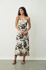 Vestido midi de tirantes finos, con escote en V y diseño cruzado estilo pareo. Presenta un estampado floral grande en tonos negros y naranjas sobre base off-white.