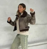 Campera corta color marrón con cuello y puños de corderito. Cierre frontal con cremallera y cintos ajustables a los lados.