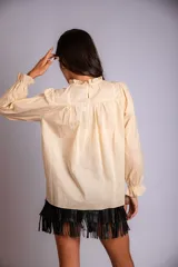 Camisa blanca de manga larga con detalles de encaje o bordado en el canesú y el frente. Presenta un corte holgado y mangas con puños elásticos o fruncidos.